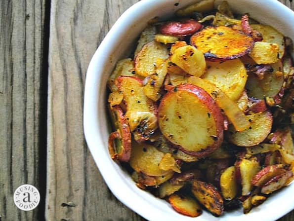 Sliced, cooked potatoes and onions in a white dish on a wooden table.
