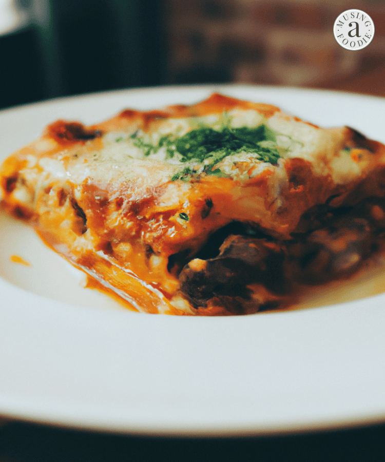 Slice of hearty beef lasagna on a white plate on top of a wooden table.