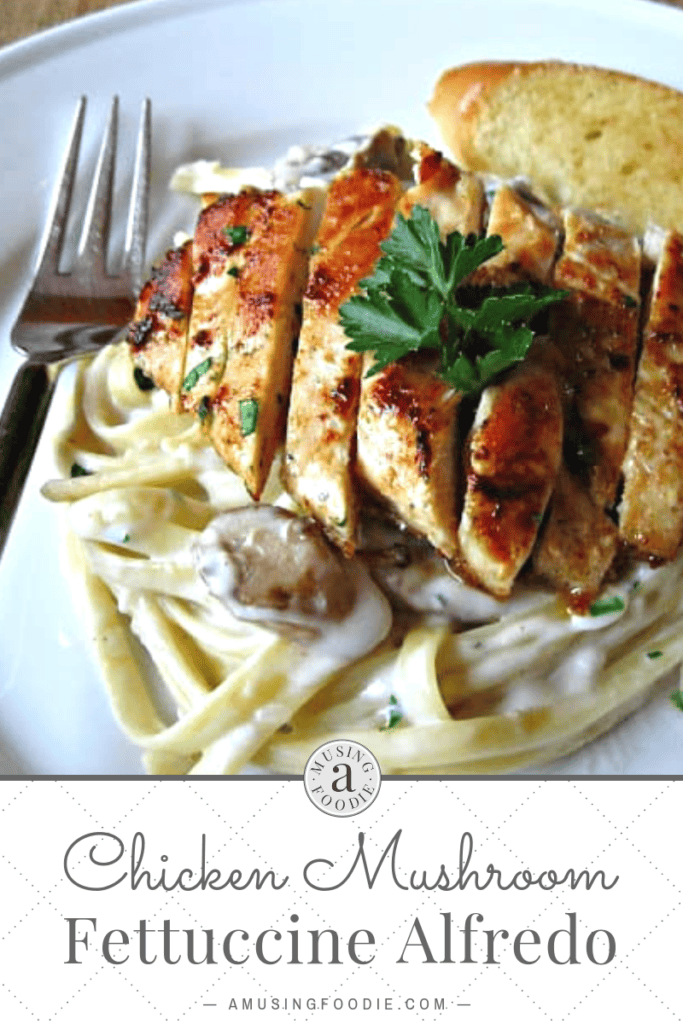 Overhead shot of sliced chicken breast on top of pasta with alfredo sauce and mushrooms. A sprig of parsley is on top and a slice of bread is in the background. A fork sits to the left.