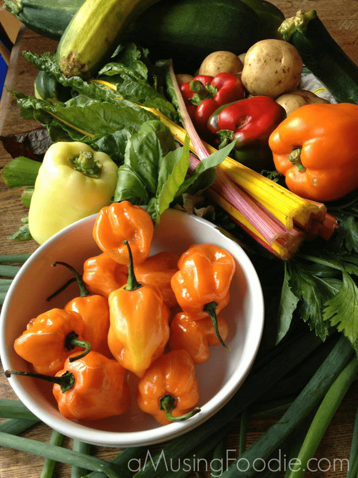 How to Make Zucchini Bread Peppers, rainbow chard, potatoes, and zucchini sitting on a wooden table. Orange peppers are in a white bowl.