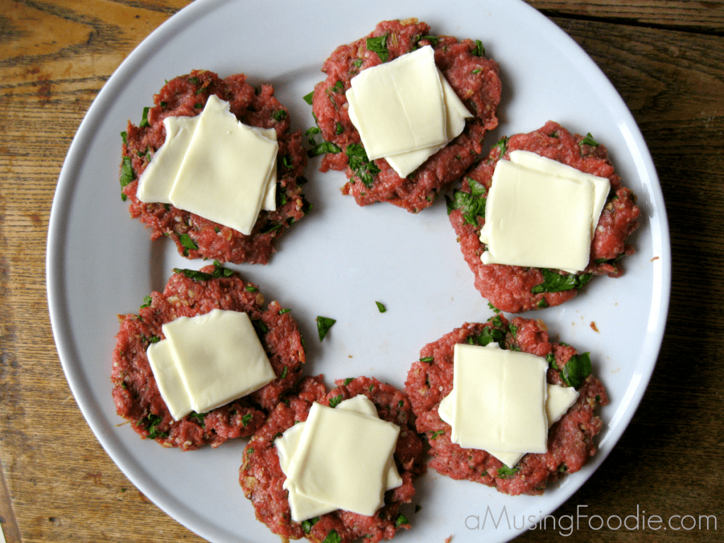 Raw slider patties on a white plate with slices of American cheese on top.