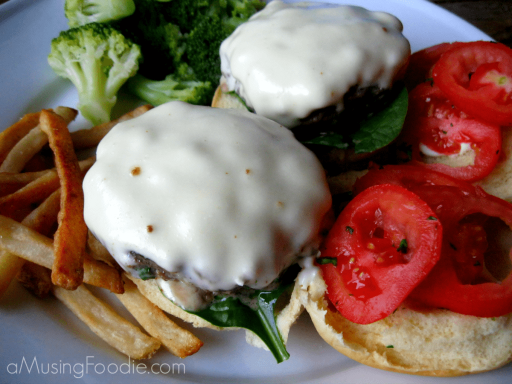 Sliders on hamburger buns covered with melted cheese, with tomato and spinach. French fries are on the side.