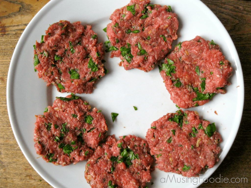 Raw slider patties on top of a white plate, sitting on a wood table.
