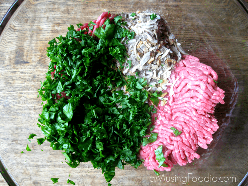 Overhead shot of raw ground beef, sliced fresh spinach and onion soup mix in a clear mixing bowl on a wooden table.