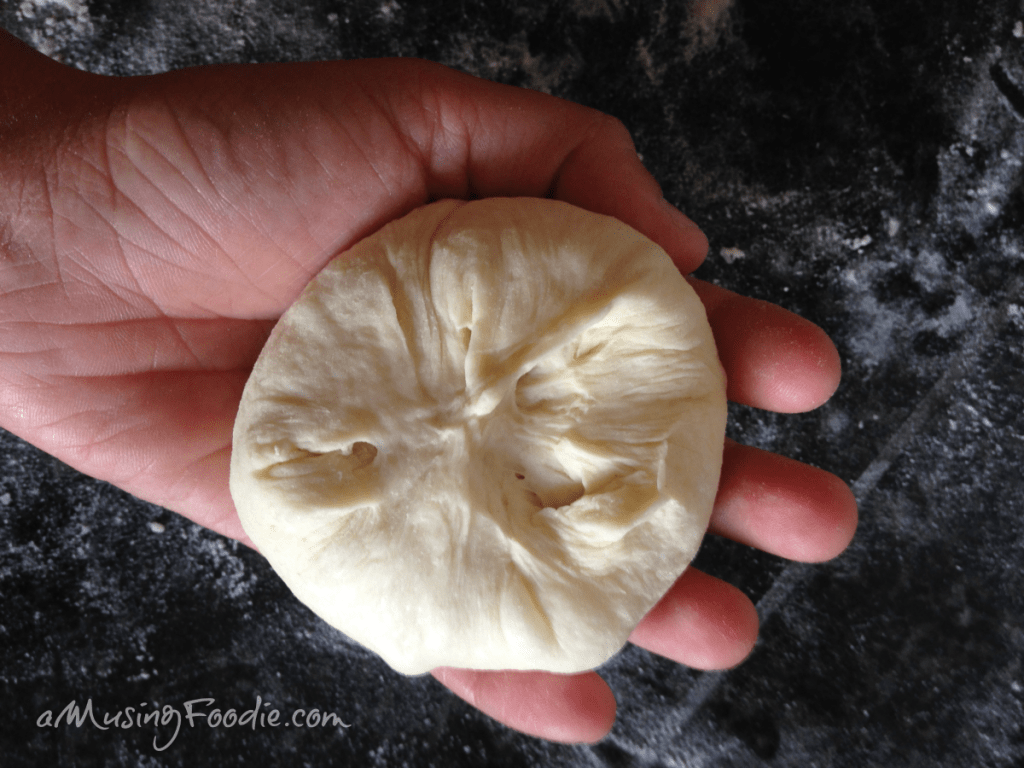 Small round of dough sitting on a hand with a dark table background.