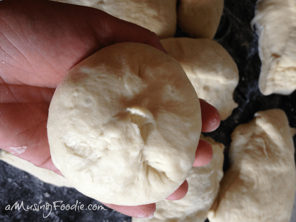 Small round of dough sitting on a hand with a dark counter in the background. More rounds of dough are on the counter.