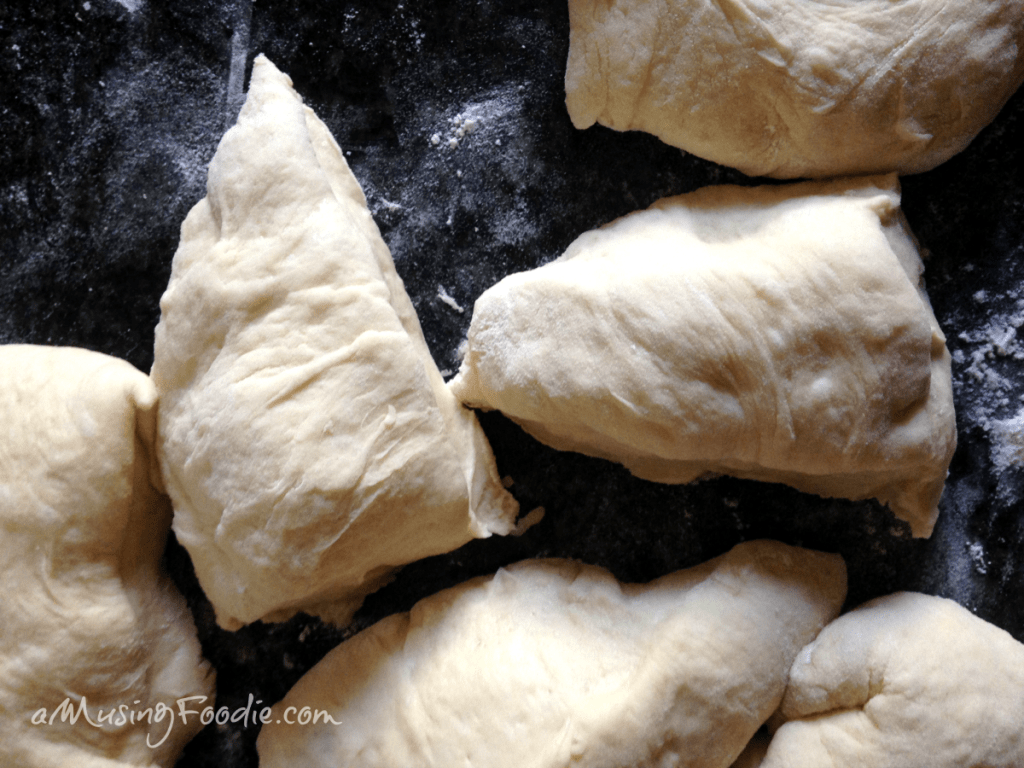 Bun dough portioned out individually on a dark backgroun.