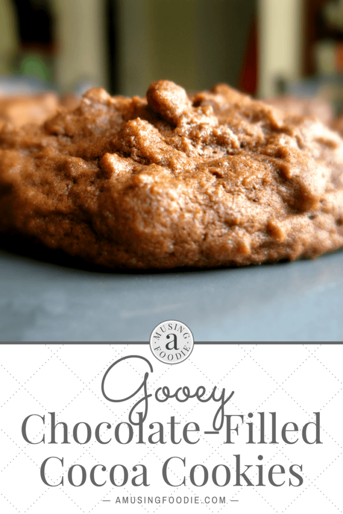 Close up side shot of a chocolate cookie on a baking sheet. Text below the image is on a white background: Gooey Chocolate-Filled Cocoa Cookies, amusingfoodie.com
