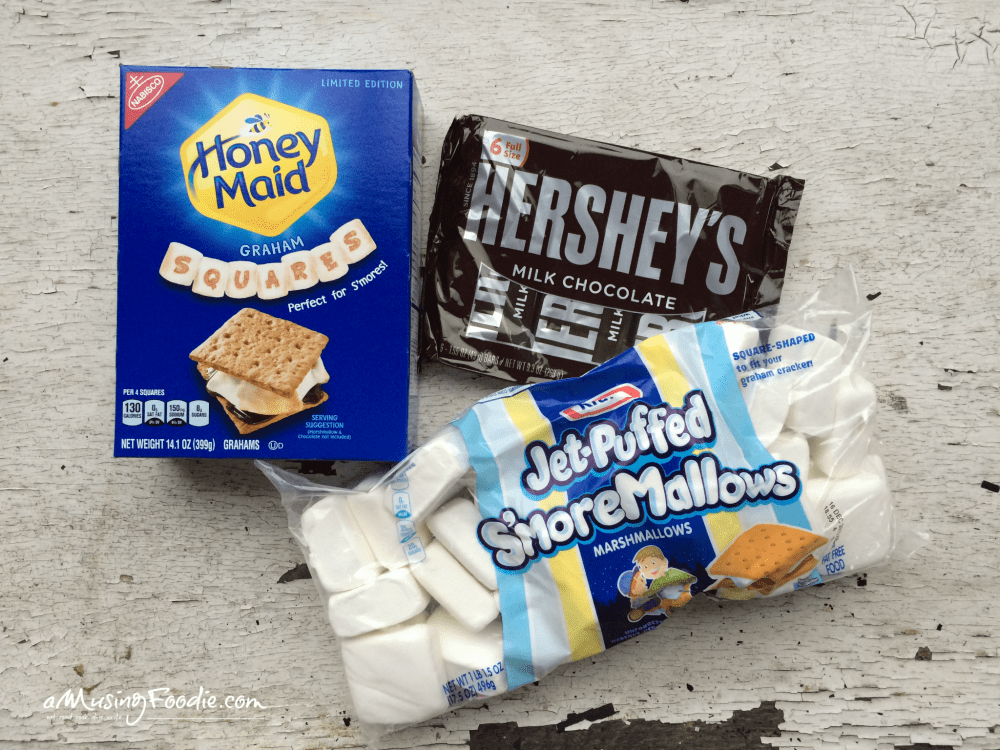 Box of graham crackers, bag of chocolate bars and bag of marshmallows laying on a table.